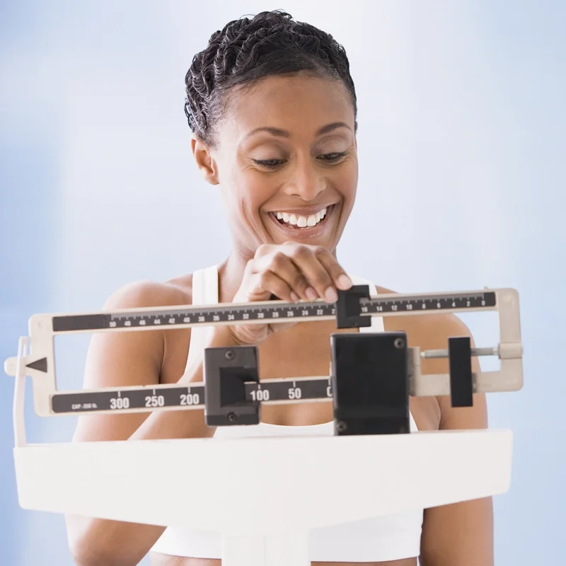 A woman using a scale smiling, happy with the result of her weight loss journey